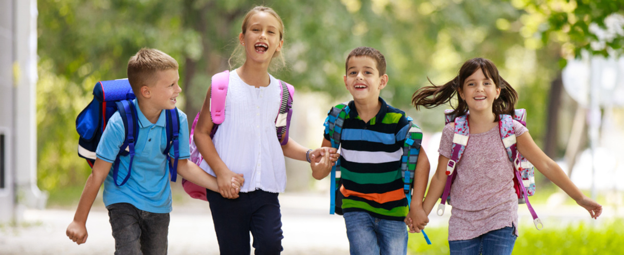Link zur Aktuelles-Meldung: Fachtag Guter Start in Klasse 1: Denkwege öffnen – mathematische Grundlagen legen! (online, 15. September 2026, 8:00 bis16:00 Uhr) (Foto: Vier Schulkinder mit Schulranzen und in Sommerkleidung laufen fröhlich lachend Hand in Hand an einem sonnigen Tag. Es handelt sich um zwei Jungen und zwei Mädchen.)