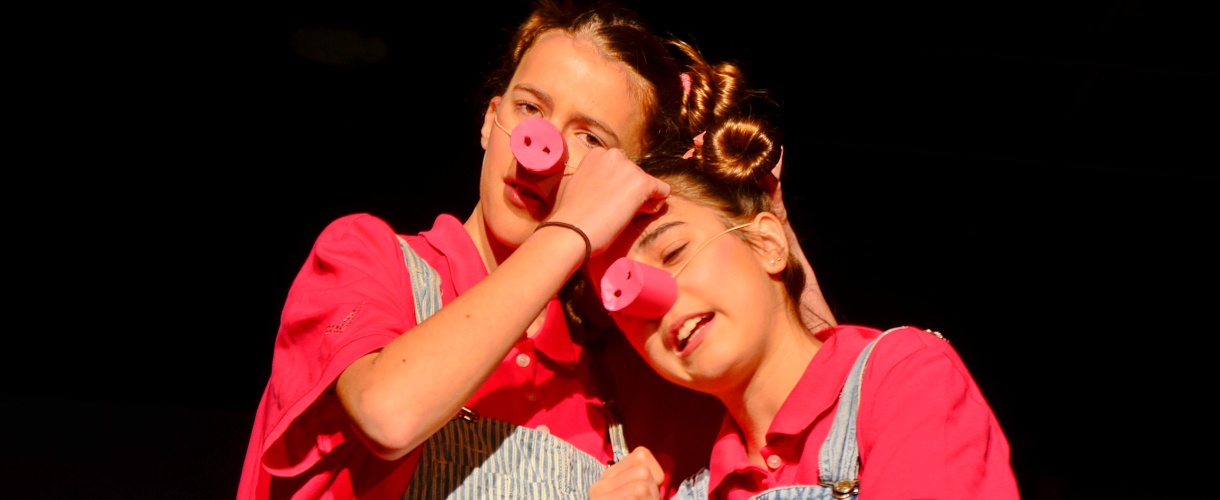Foto einer Szene: Zwei Jugendliche mit rosa Pappnasen legen die Köpfe zusammen.
