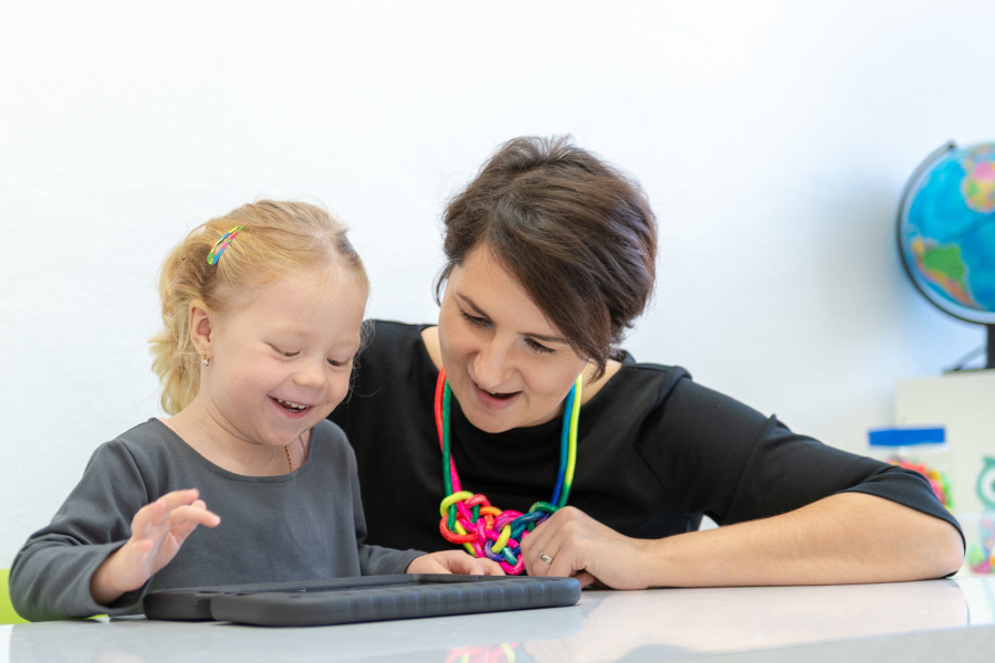 Link zur Seite Kommunikation in der Sonderpädagogik (Foto: Sonderpädagogin mit Kleinkind; Kind kommuniziert mittels technischer Hilfe)