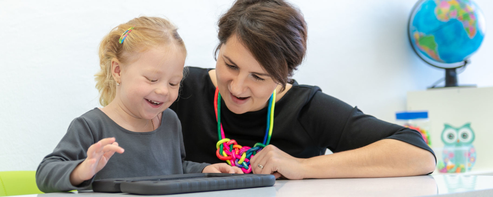 Foto: Sonderpädagogin mit Kleinkind; Kind kommuniziert mittels technischer Hilfe