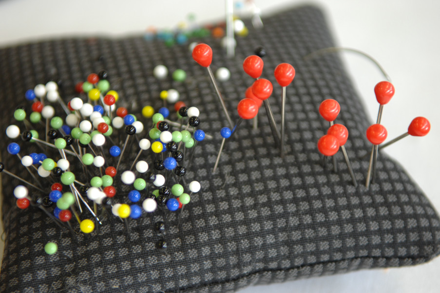 Link zur ZSL-Seite „Hauswirtschaft“; Foto: Bunte Stecknadeln stecken in einem karrierten Nadelkissen.