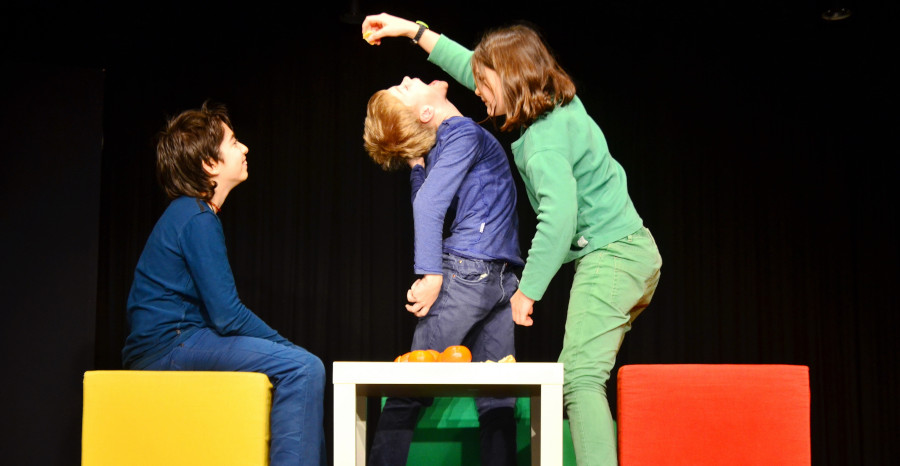 Link zur ZSL-Seite „Schülergruppen Theater“; Foto einer Schultheaterszene: drei einfarbig gekleidete Kinder agieren vor dunklem Hintergrund.