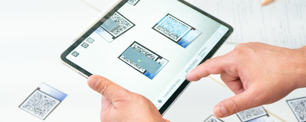 Symbolbild für Augmented Reality (Foto: QR-Codes werden mit einem Tablet abgescannt; sichtbar sind zwei Hände, ein Tablet und Codes)