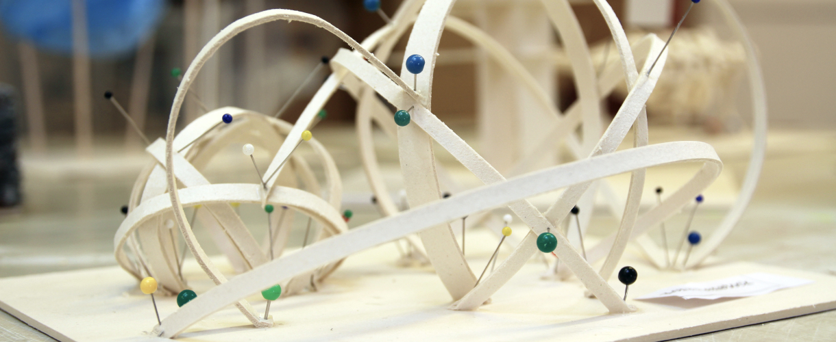 Foto: Abstraktes Raummodell aus hellen, gebogenen Papierstreifen, die durch bunte Stecknadeln fixiert sind.