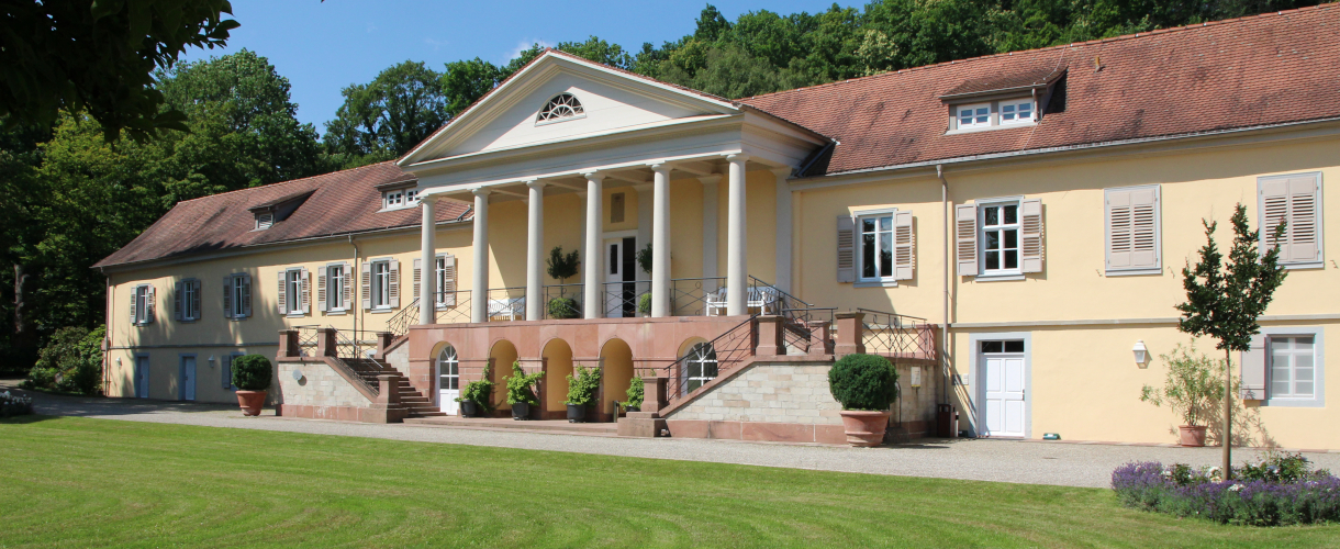 Foto: Blick über den grünen Rasen auf die Fassade von Schloss Rotenfels bei Sonnenschein.