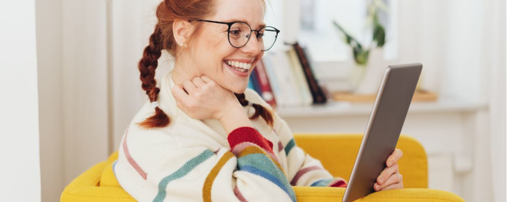 Foto: Eine Lehrerin schaut lachend auf ein Tablet, das sie in der Hand hält.