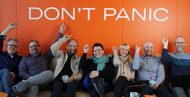 Foto: Das Kernteam des KI-Zentrums Schule sitzt vor orangefarbener Wand mit weißem Schriftzug 