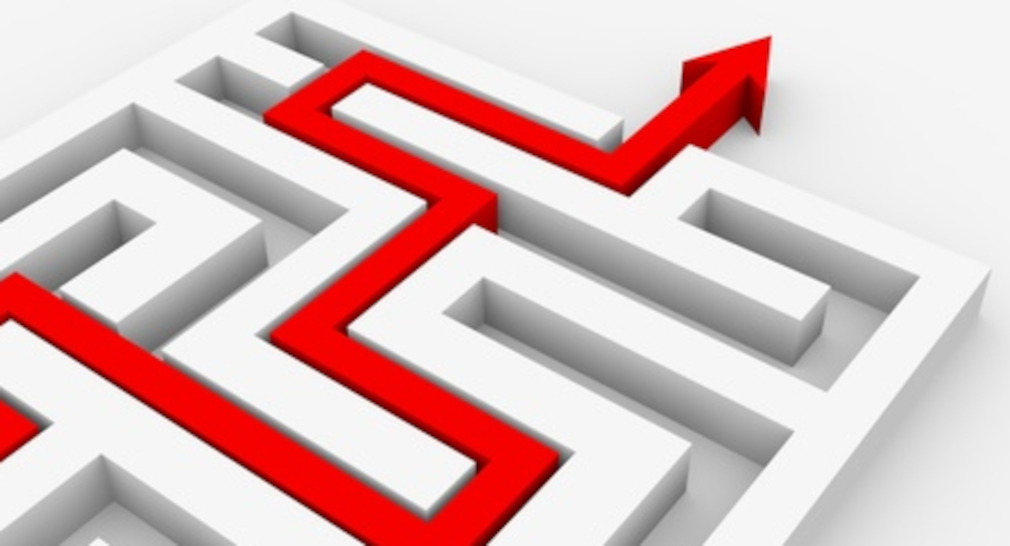 Symbolbild Schulentwicklung: In einem weißen dreidimensionalen Labyrinth liegt ein verwinkelter, langer roter Pfeil, der oben rechts im Bild aus dem Labyrinth tritt.